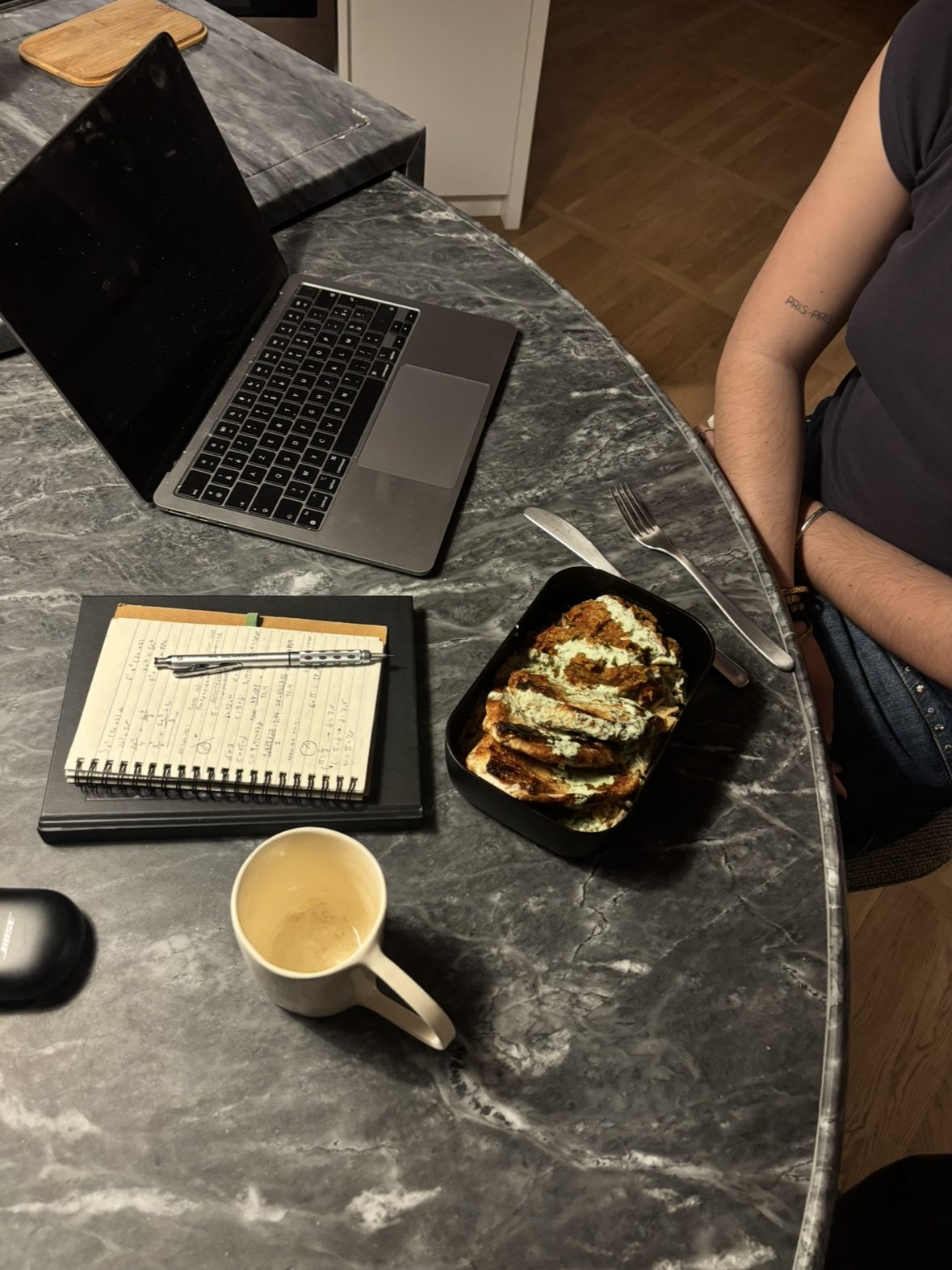 A packed meal prep container beside a laptop and notebook on a stone desk